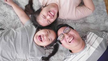 Vista superior de la feliz familia asiática tirada en el suelo de la sala de estar, mirando a la cámara y riendo juntos. quedarse con la familia en casa durante el fin de semana. concepto de familia feliz video