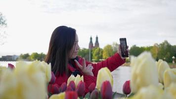 mulher asiática caminhando e sentada para tirar uma selfie com lindas flores, tulipas, no parque da cidade, ficando um momento maravilhoso, sentindo-se relaxar e vendo a beleza natural. fundo do parque da cidade video