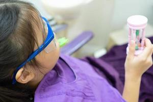 Young Girl Holding Hour Glass While Doing Fluoride Treatment in Dental Clinic photo