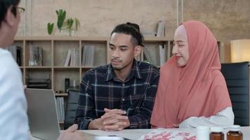 People medical insurance clinic service. Young Muslim couple discussing and consulting with a professional Asian male doctor about his wife's health who is a beautiful woman wears a hijab in office. video