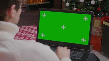 hombre usando laptop con pantalla verde de maqueta en una habitación temática navideña.