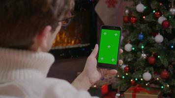 man kijken op groen scherm telefoon in een kamer met kerstthema. video