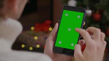 Man scrolling on green screen phone in a Christmas themed room. video