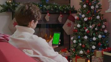 homme tenant un smartphone avec écran vert sur fond de Noël avec des cadeaux.