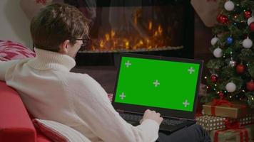 El hombre tiene una videollamada con su familia en una computadora portátil de pantalla verde en una habitación temática navideña. video