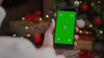 Greenscreen-Vorlagen-Smartphone in Mannhänden im Weihnachtsinnenraum zu Hause.