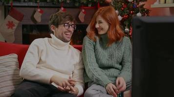 couple souriant devant la télévision dans une salle sur le thème de Noël.