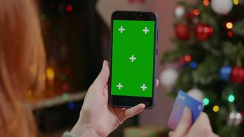 mujer está comprando en línea con un teléfono móvil en una sala de temática navideña. video