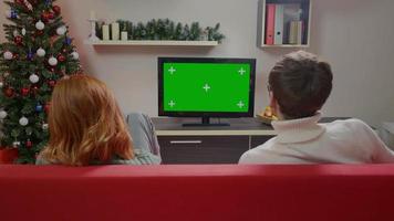 paar kijken naar een groen scherm tv in de woonkamer tijdens de kerstperiode. video