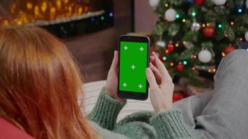 mulher segurando um telefone celular com um fundo chave de croma de tela verde no interior do Natal.