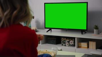 mujer sentada en el sofá viendo la televisión de pantalla verde. video