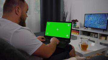 Mann mit Laptop mit grünem Bildschirm und Bier trinken. video
