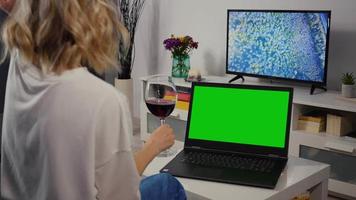 la donna ha una videochiamata con lo schermo verde del laptop acceso con un amico mentre beve un bicchiere di vino video