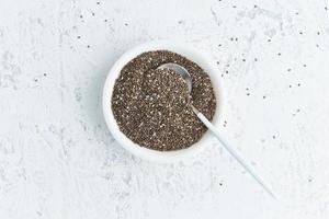 Chia seeds in white bowl on white stone concrete background, top view, copy space photo