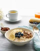 Whole oatmeal, large bowl of porridge with banana, berries, nuts for breakfast. Side view, vertical photo