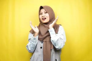 Hermosa joven mujer musulmana asiática conmocionada, sorprendida, expresión guau, con la mano que sostiene la mejilla frente a la cámara aislada sobre fondo amarillo