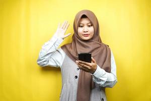 Hermosa joven musulmana asiática conmocionada, sorprendida, con las manos sosteniendo el teléfono inteligente, mirando el teléfono inteligente, mirando la promoción, aislado sobre fondo amarillo, concepto de publicidad foto