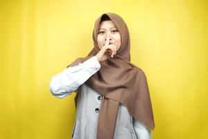 Hermosa joven musulmana asiática con el dedo en la boca, diciendo que se calle, no hagas ruido, baja la voz, no hables, aislado sobre fondo amarillo