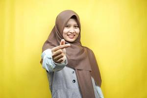 Beautiful young asian muslim woman smiling, with korean love sign hand, hand close to camera, isolated on yellow background photo