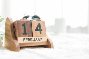 Cerca del calendario de madera que muestra el día de San Valentín rodeado de cálida luz solar. evento del día de San Valentín de amante en el dormitorio blanco. foto