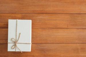 Navidad y año nuevo caja de regalo envuelta con papel blanco y lazo de cinta en la mesa de madera - vista superior sobre fondo de mesa de madera. foto