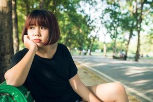 Young Asian woman sitting outdoor on the public bench and lying along the bench in the park in warm sunlight day. Young Woman relax her mind and body in the park. Outdoor activity in the park concept.