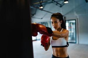 Joven mujer asiática kickboxing ejercicio entrenamiento saco de boxeo luchador femenino duro práctica de boxeo en clase de gimnasia. deportista actividad recreativa, entrenamiento funcional, concepto de estilo de vida saludable.