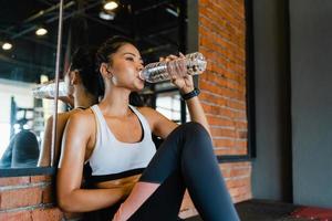 Hermosa joven asiática ejercicio agua potable después de ejercicios para quemar grasa en la clase de gimnasia. atleta con six pack, actividad recreativa deportista, entrenamiento funcional, concepto de estilo de vida saludable. foto