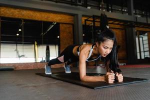 Ejercicio feliz de la señora joven de Asia que hace ejercicios quemagrasas del tablón en la clase de gimnasia. atleta con six pack, actividad recreativa deportista, entrenamiento funcional, concepto de estilo de vida saludable. foto