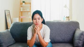 Depressed crying Asian business woman stressed with headache sitting on sofa in living room at house when social distancing stay at home and self quarantine time, coronavirus concept.