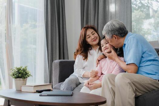 abuelos asiáticos besan la mejilla de la nieta en casa. Los chinos mayores, la generación anterior, el abuelo y la abuela que usan el tiempo en familia se relajan con la niña acostada en el sofá en el concepto de sala de estar. foto