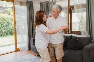 Asian elderly couple dancing together while listen to music in living room at home, sweet couple enjoy love moment while having fun when relaxed at home. Lifestyle senior family relax at home concept. photo