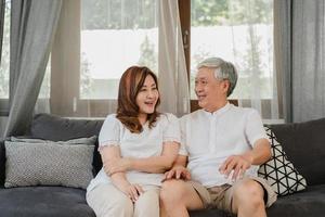 Asian senior couple relax at home. Asian Senior Chinese grandparents, husband and wife happy smile hug talking together while lying on sofa in living room at home concept. photo