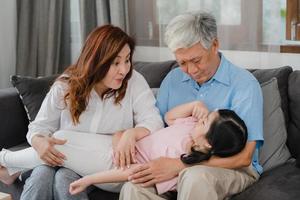 abuelos asiáticos hablando con su nieta en casa. Los chinos mayores, la generación anterior, el abuelo y la abuela que usan el tiempo en familia se relajan con la niña acostada en el sofá en el concepto de sala de estar. foto