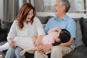 abuelos asiáticos hablando con su nieta en casa. Los chinos mayores, la generación anterior, el abuelo y la abuela que usan el tiempo en familia se relajan con la niña acostada en el sofá en el concepto de sala de estar. foto