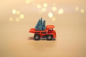 Orange truck with Christmas trees on a beige background with lights. Holidays concept. Close up, with copy space. photo
