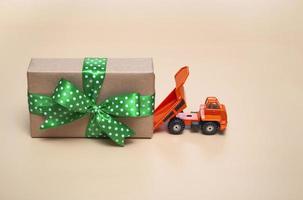 Orange truck with a large gift on a beige background. Holidays concept. With close up, copy space. photo