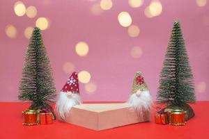 Festive concept. On a colored background in lights, a podium for cosmetics and various goods with gnomes, gifts and Christmas trees. Close up with copy space photo