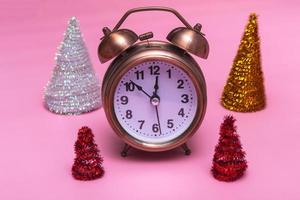 Christmas or New Years minimal concept. Alarm clock and multicolored Christmas trees on a pink background. photo