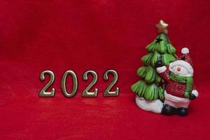 Concept for New Year's card, invitation and packaging on a fabric red background a snowman with a Christmas tree and golden numbers 2022 photo