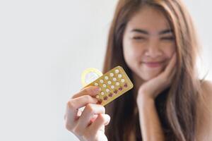 Young woman holding condom and contraceptive pills prevent pregnancy photo