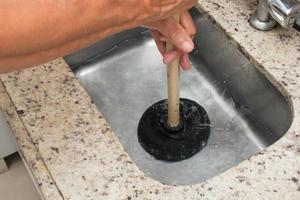 Hombre usando un desatascador para destapar el fregadero de la cocina foto