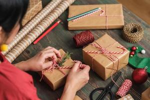 woman making Christmas handmade gift box with brown paper warpping with xmas decor on wood table photo