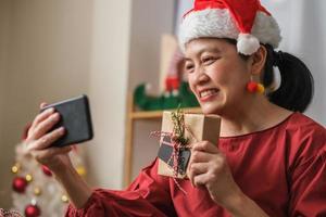 asian woman wear santa hat video call party with friends with mobile phone on table at home