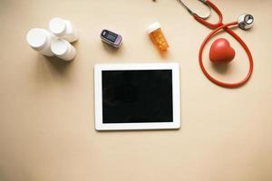 digital tablet, stethoscope and pill container on table