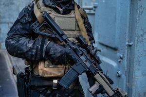 Soldado moderno en uniforme negro multicámara con rifle, fondo urbano foto