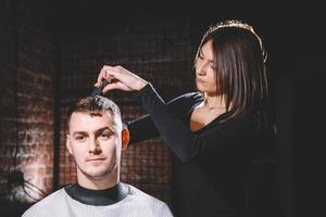 Hermosa peluquera cortando el cabello del cliente con unas tijeras en una peluquería foto