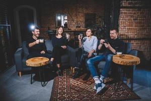 Cheerful guys and girls are sitting on sofa with cups in hands photo