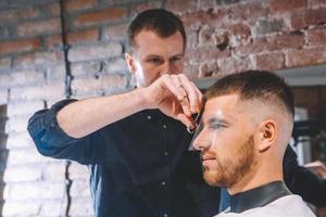 Barbero masculino afeita la cabeza del cliente con una recortadora eléctrica