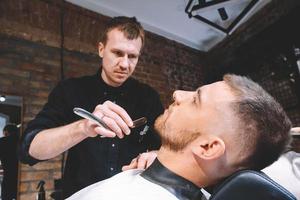 Barbero masculino hace un cliente de barba de corte de pelo con navaja de afeitar recta vintage